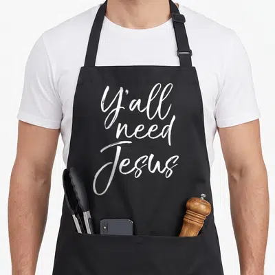 Jesus southern aprons - White stacked script text reading Y'all need Jesus — shown on a black cotton canvas apron against a white background