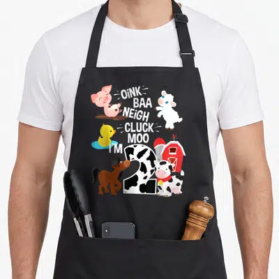 Baa farm apron - Cartoon number 2 with cow spots, farm animals, red barn, and stacked animal sound text — shown on a black cotton canvas apron against a white background