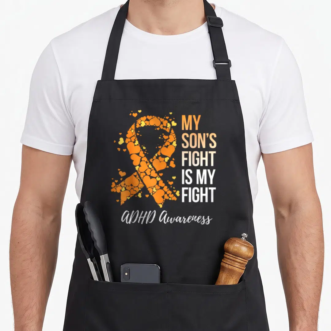Son adhd apron - Orange and white awareness ribbon formed by hearts next to stacked text and ADHD Awareness script — shown on a black cotton canvas apron against a white background