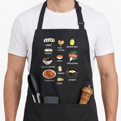 Food korean apron - Cartoon GIMBAP, FRIED CHICKEN, BANANA MILK, and other Korean foods with grey labels on black — shown on a black cotton canvas apron against a white background