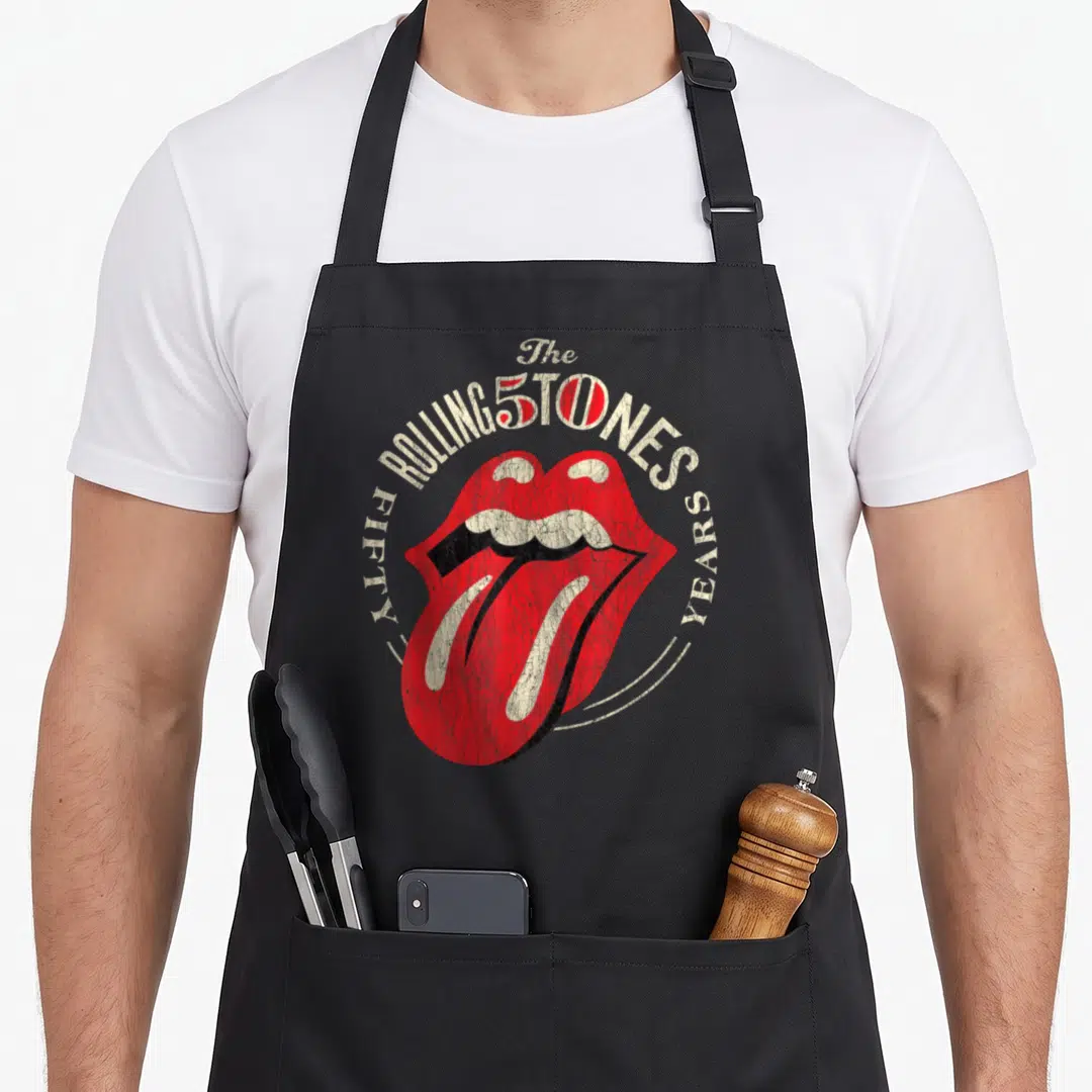 50th rolling stones apron - Red lips and tongue logo with circular FIFTY YEARS text in cream and black distressed style — shown on a black cotton canvas apron against a white background