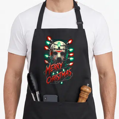 Festive candy cane apron - Hockey mask wrapped in red and green lights with MERRY CHRISTMAS text — shown on a black cotton canvas apron against a white background