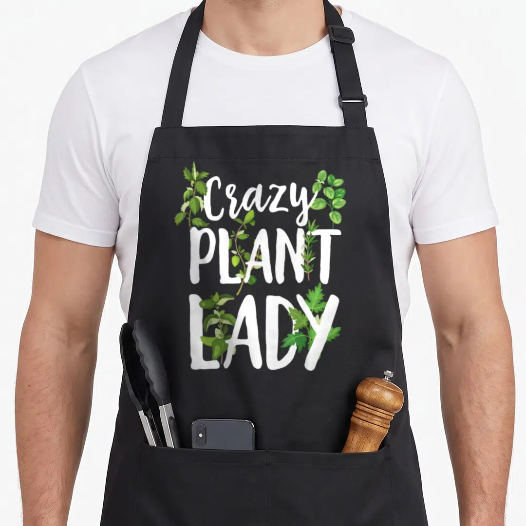 Cool gardening plant lady apron - Stacked white text Crazy Plant LADY with green leaves woven through the letters — shown on a black cotton canvas apron against a white background