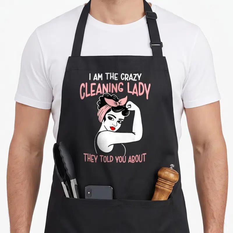 Housekeeping cleaning lady apron - Retro cartoon woman flexing with pink text I AM THE CRAZY CLEANING LADY THEY TOLD — shown on a black cotton canvas apron against a white background
