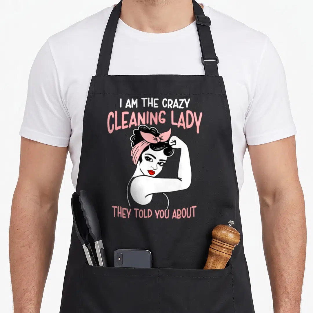 Housekeeping cleaning lady apron - Retro cartoon woman flexing with pink text I AM THE CRAZY CLEANING LADY THEY TOLD — shown on a black cotton canvas apron against a white background