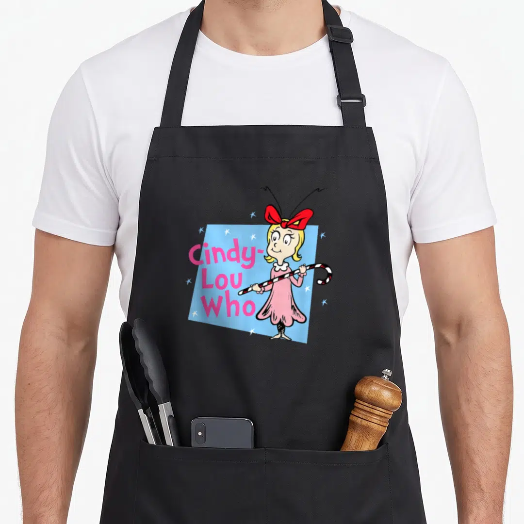 Funny holiday cindy lou who apron - Cindy-Lou Who character holding candy cane next to pink stacked text on blue — shown on a black cotton canvas apron against a white background
