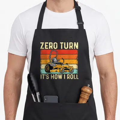 Zero gardener apron - Retro yellow zero-turn mower on red orange and teal stripes with text — shown on a black cotton canvas apron against a white background