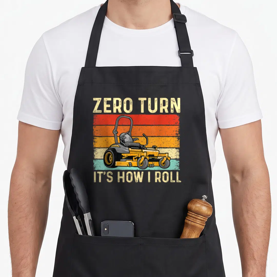 Zero gardener apron - Retro yellow zero-turn mower on red orange and teal stripes with text — shown on a black cotton canvas apron against a white background