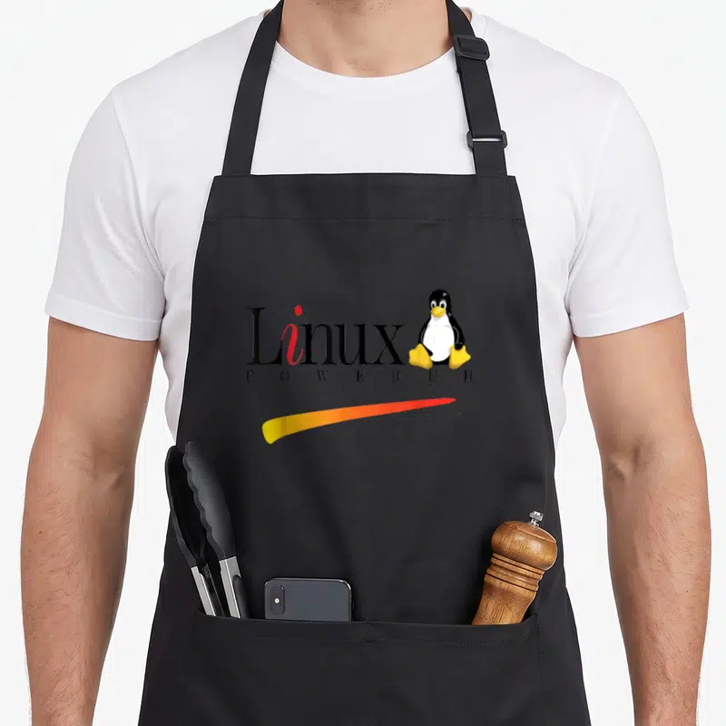 Linux penguin aprons - Cartoon penguin sitting next to Linux text with gradient swoosh — shown on a black cotton canvas apron against a white background