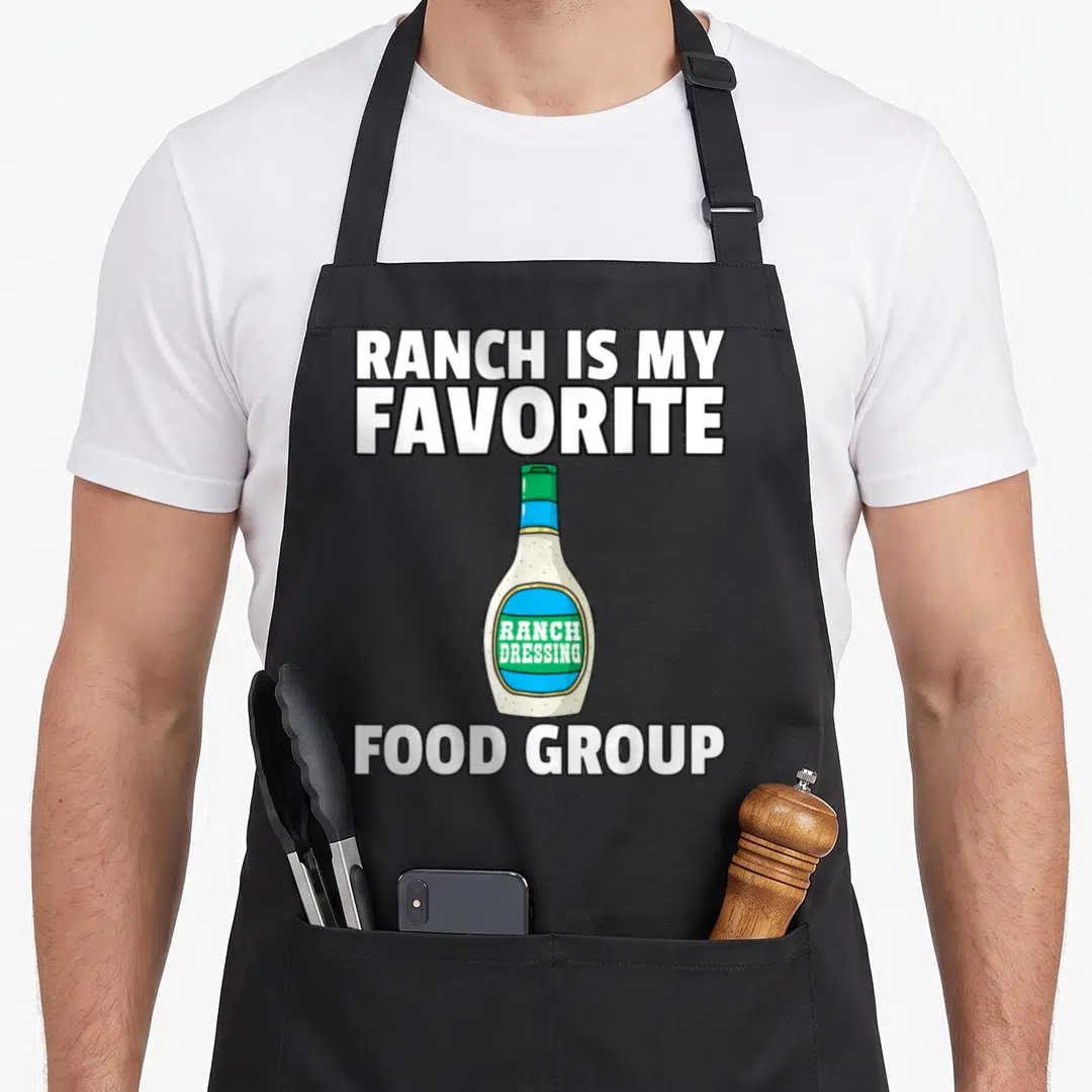 Ranch condiment dressing apron - Cartoon ranch bottle between 'Ranch Is My Favorite' and 'Food Group' text — shown on a black cotton canvas apron against a white background