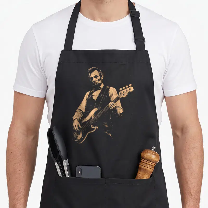 Bassist playing guitar apron - Tan distressed image of Abraham Lincoln playing a bass guitar — shown on a black cotton canvas apron against a white background