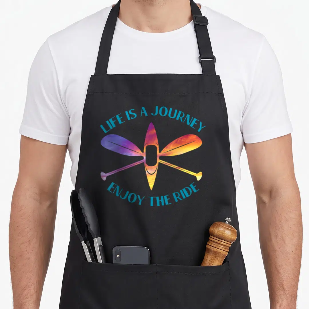 Journey kayak apron - Colorful kayak and crossed paddles with Life is a Journey Enjoyn the Ride text — shown on a black cotton canvas apron against a white background