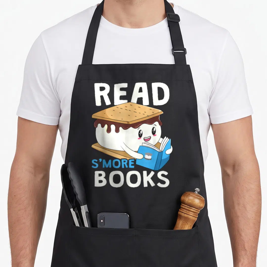 Bookworm camping apron - Cartoon s'more character reading a blue book with text READ S'MORE BOOKS — shown on a black cotton canvas apron against a white background