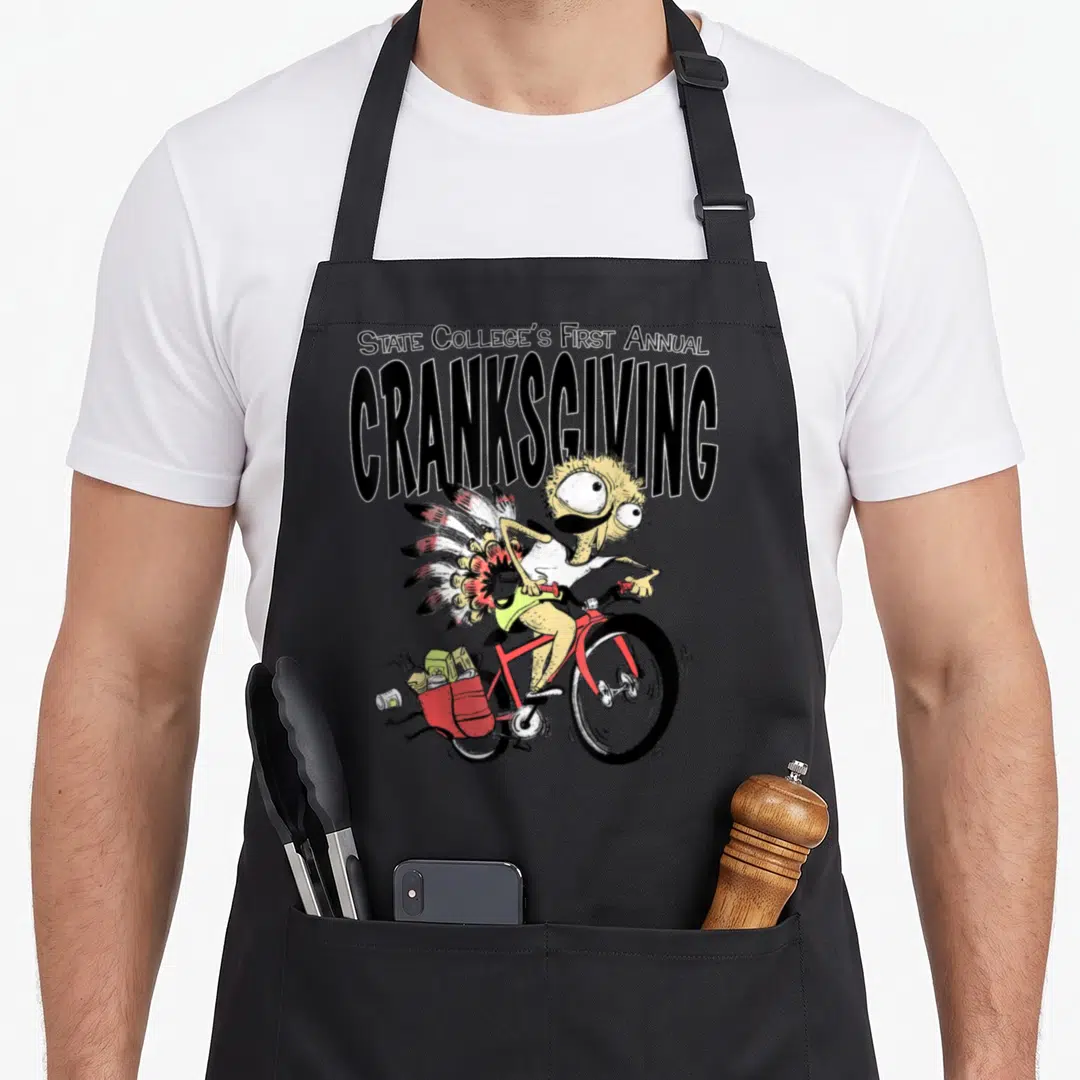 Cranksgiving state college apron - Stacked text above cartoon cyclist with turkey tail and red grocery bag — shown on a black cotton canvas apron against a white background