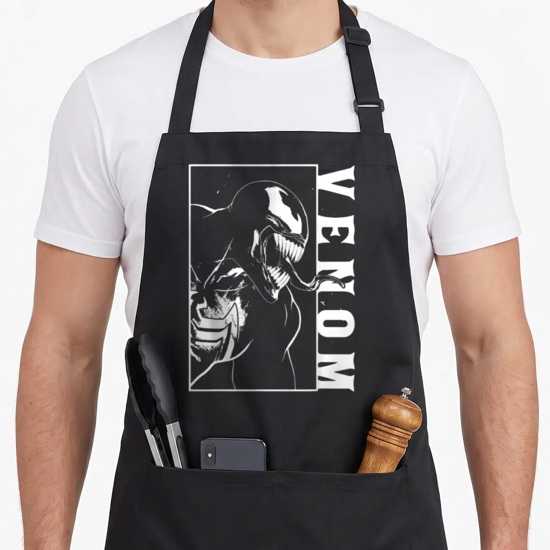 View comics apron - White line art Venom character in a rectangular frame with vertical text on black fabric — shown on a black cotton canvas apron against a white background