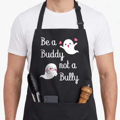 Bully buddy aprons - Be a Buddy not a Bully text with happy and angry white ghosts and pink hearts — shown on a black cotton canvas apron against a white background