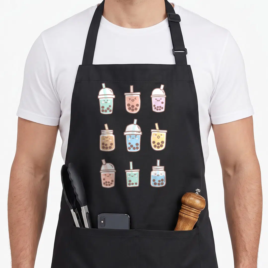 Boba anime cooking apron - Nine cartoon bubble tea cups with faces in mint, pink, purple, yellow, and light blue — shown on a black cotton canvas apron against a white background