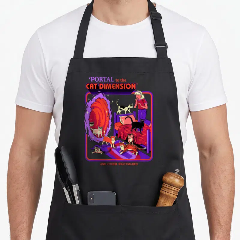 Steven cat apron - Cartoon woman and cats near swirling portal with purple border and red text — shown on a black cotton canvas apron against a white background