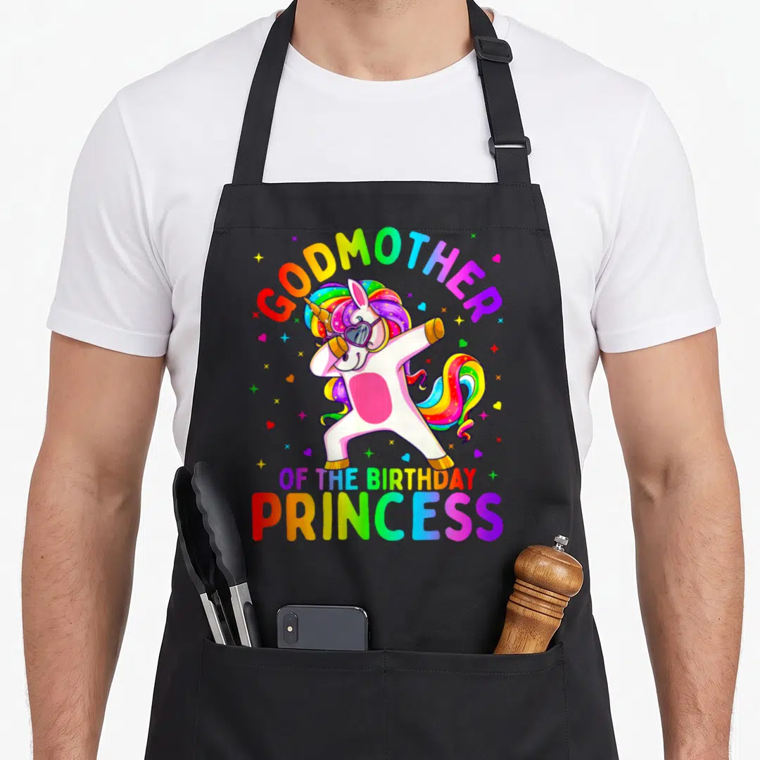 Godmother princess apron - Dabbing unicorn with rainbow GODMOTHER OF THE BIRTHDAY PRINCESS text and scattered hearts — shown on a black cotton canvas apron against a white background