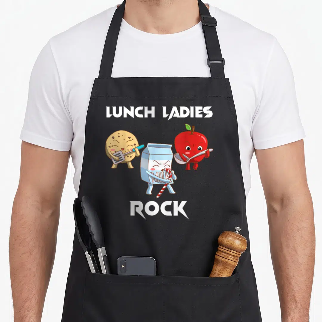 Funny rock lunch lady apron - Three cartoon food characters holding utensils under LUNCH LADIES ROCK text — shown on a black cotton canvas apron against a white background