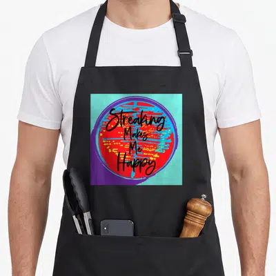 Lab microbiologist apron - Streaking Makes Me Happy text over red blue yellow circle with purple border — shown on a black cotton canvas apron against a white background