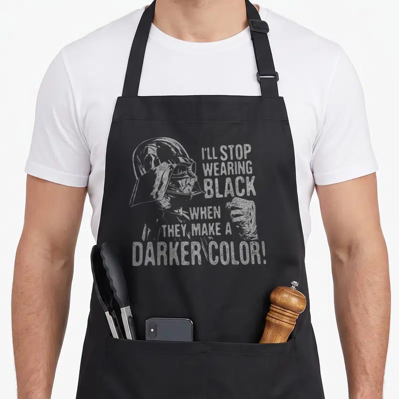 Stop general apron - Darth Vader profile with I'll stop wearing black when they make a darker color text — shown on a black cotton canvas apron against a white background