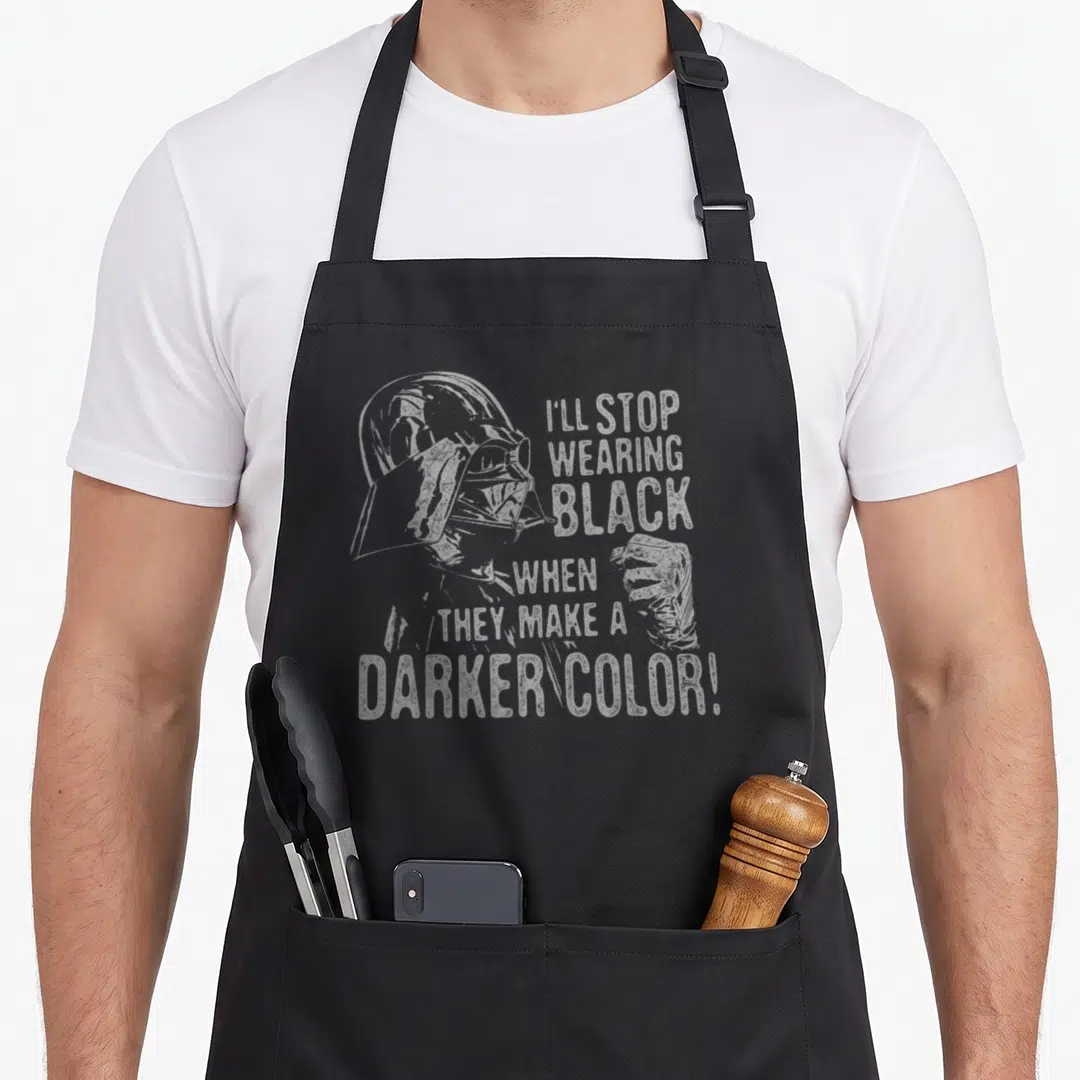 Stop general apron - Darth Vader profile with I'll stop wearing black when they make a darker color text — shown on a black cotton canvas apron against a white background