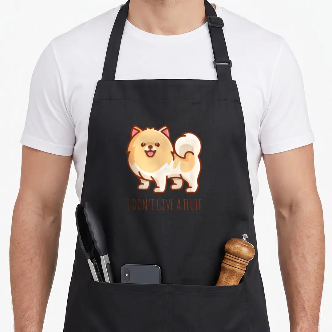 Pom pomeranian apron - Cartoon Pomeranian dog illustration with text I DON'T GIVE A FLUFF below — shown on a black cotton canvas apron against a white background