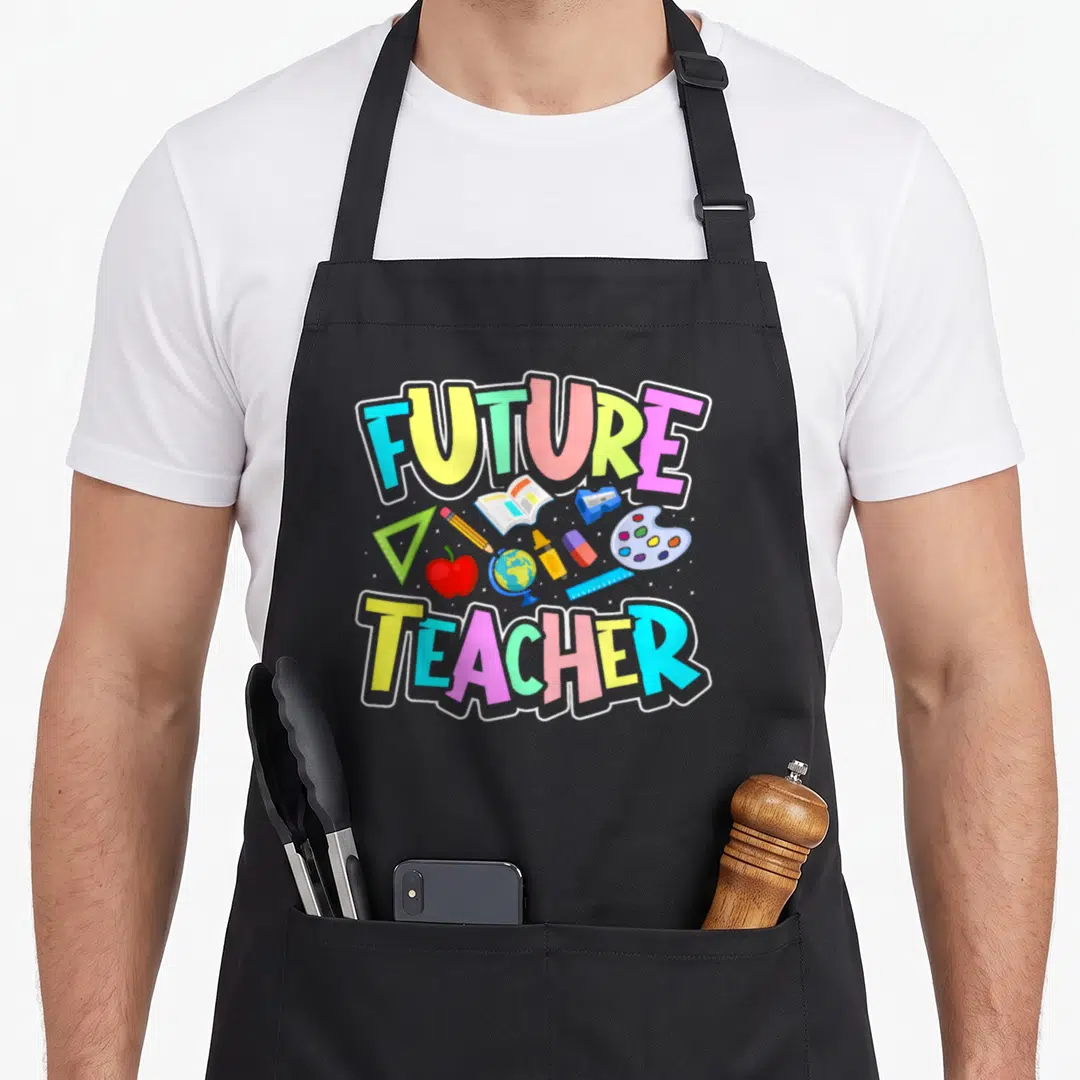 Future career teacher apron - FUTURE TEACHER text with apple globe pencil ruler sharpener eraser crayon palette — shown on a black cotton canvas apron against a white background