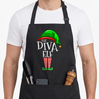 Wife christmas elf apron - The Diva Elf text with green hat and red white striped legs — shown on a black cotton canvas apron against a white background