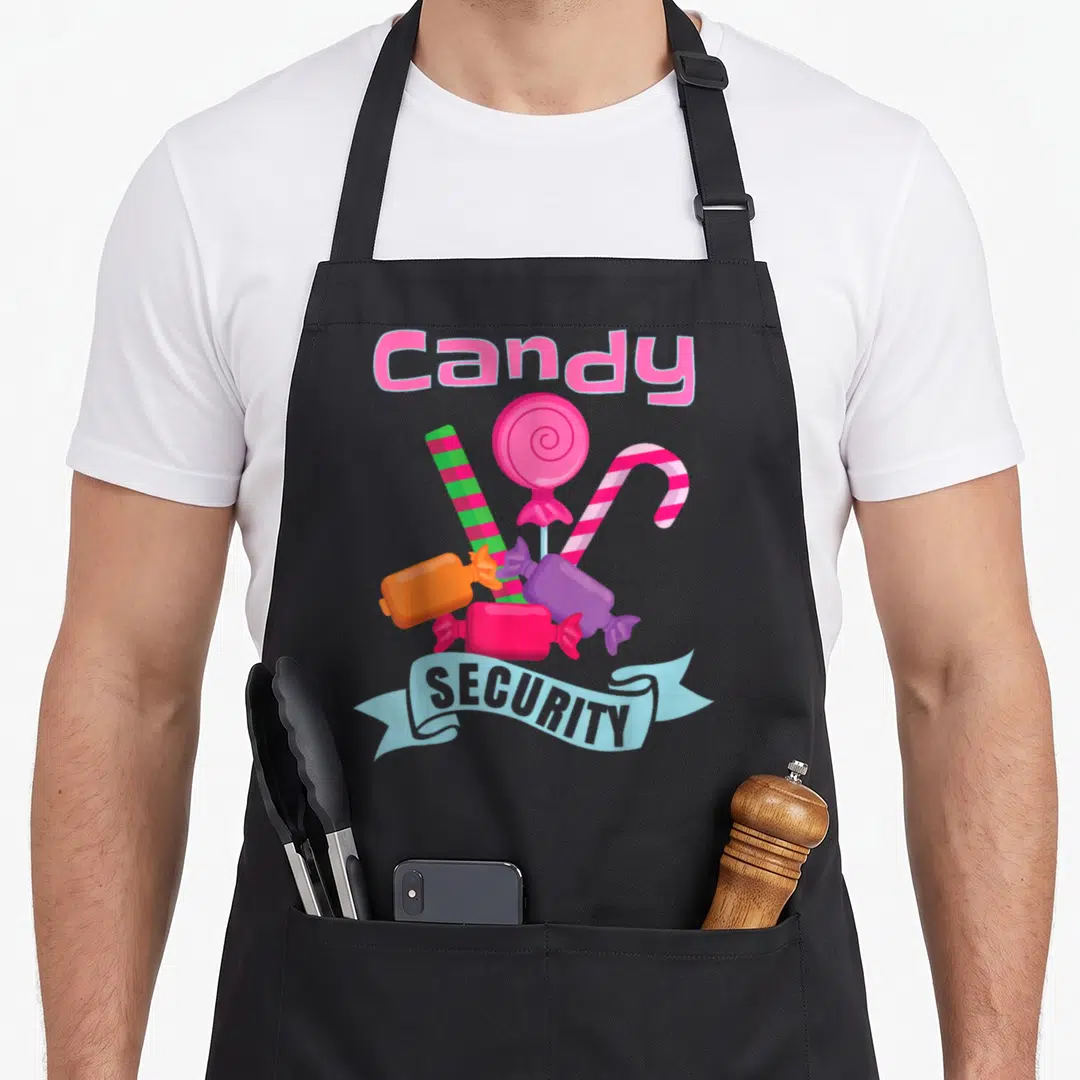 Candy security halloween apron - Cartoon graphic of pink lollipop, striped stick, and purple wrappers under a blue — shown on a black cotton canvas apron against a white background