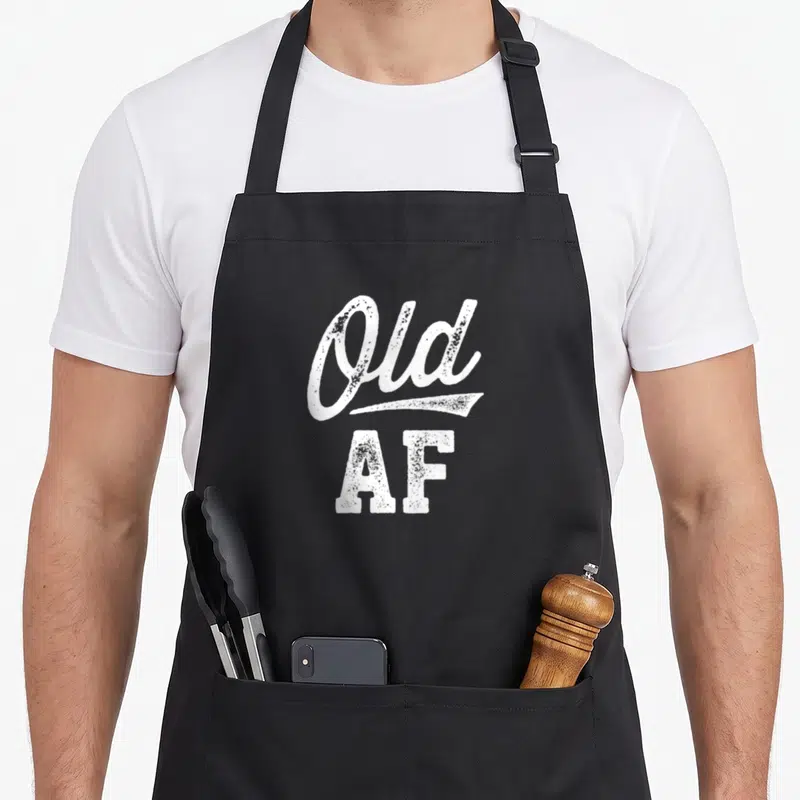 Hill birthday apron - White distressed Old AF typography on black background — shown on a black cotton canvas apron against a white background