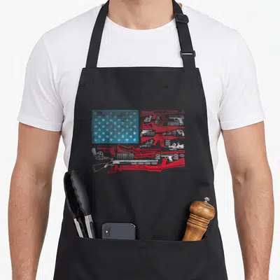 Bullet american flag apron - Distressed flag design with red and white stripes formed by firearms and a blue star field — shown on a black cotton canvas apron against a white background