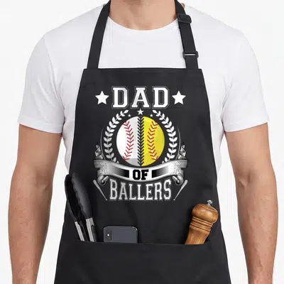 Cute baller baseball apron - DAD OF BALLERS text with split white yellow ball wreath and bats — shown on a black cotton canvas apron against a white background