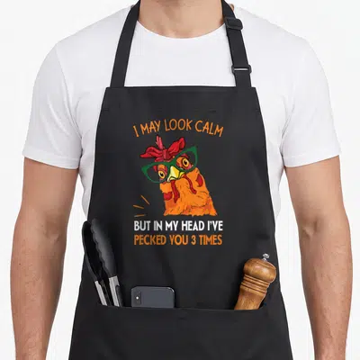 Pecked i love my rooster apron - Cartoon chicken head with green glasses and sarcastic text about pecking three times — shown on a black cotton canvas apron against a white background