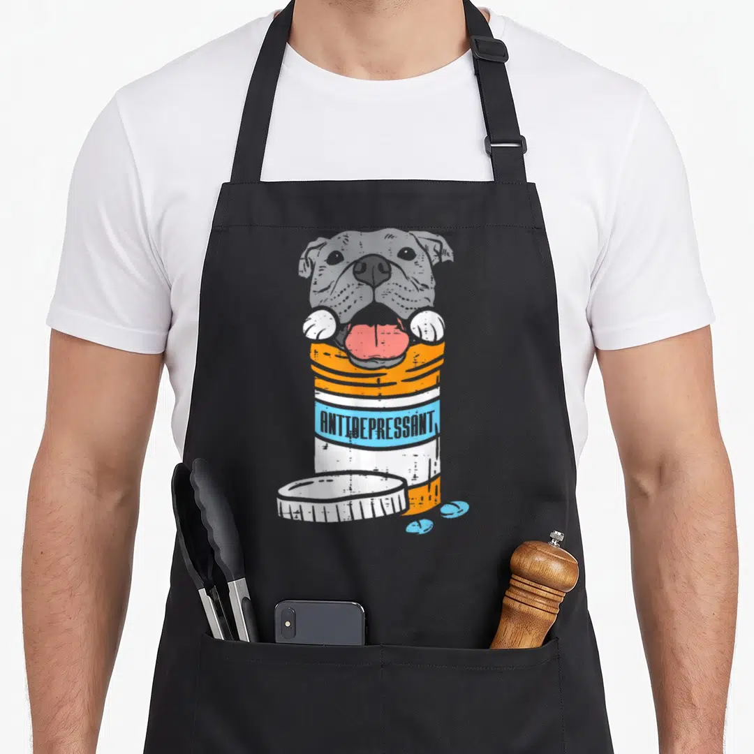 Antidepressant custom dog apron - Grey dog head in orange pill bottle with blue ANTIDEPRESSANT text and three pills — shown on a black cotton canvas apron against a white background