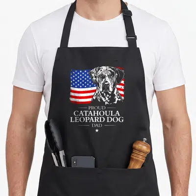 Flag leopard apron - Distressed USA flag behind grey dog portrait with Proud Catahoula Leopard Dog Dad text — shown on a black cotton canvas apron against a white background