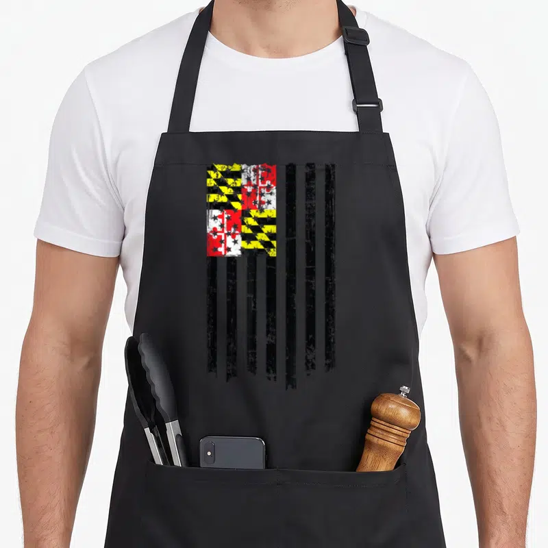Maryland american flag apron - Distressed black yellow red white flag design with Calvert cross pattern and vertical — shown on a black cotton canvas apron against a white background
