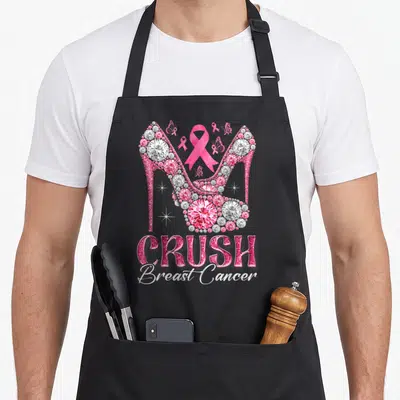 Crush ribbon apron - Two pink diamond high heels with ribbons and CRUSH Breast Cancer text — shown on a black cotton canvas apron against a white background