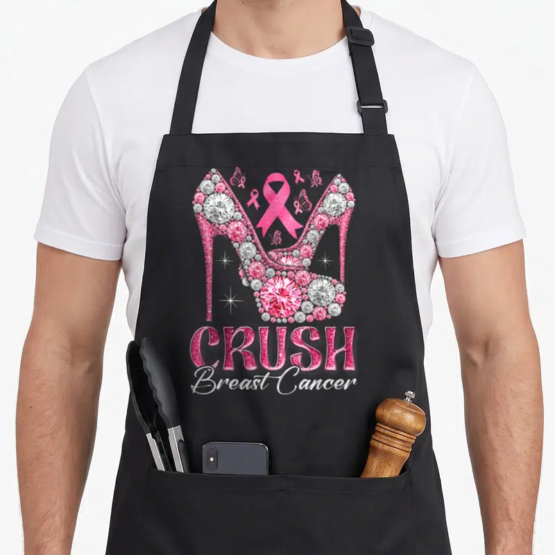 Crush ribbon apron - Two pink diamond high heels with ribbons and CRUSH Breast Cancer text — shown on a black cotton canvas apron against a white background