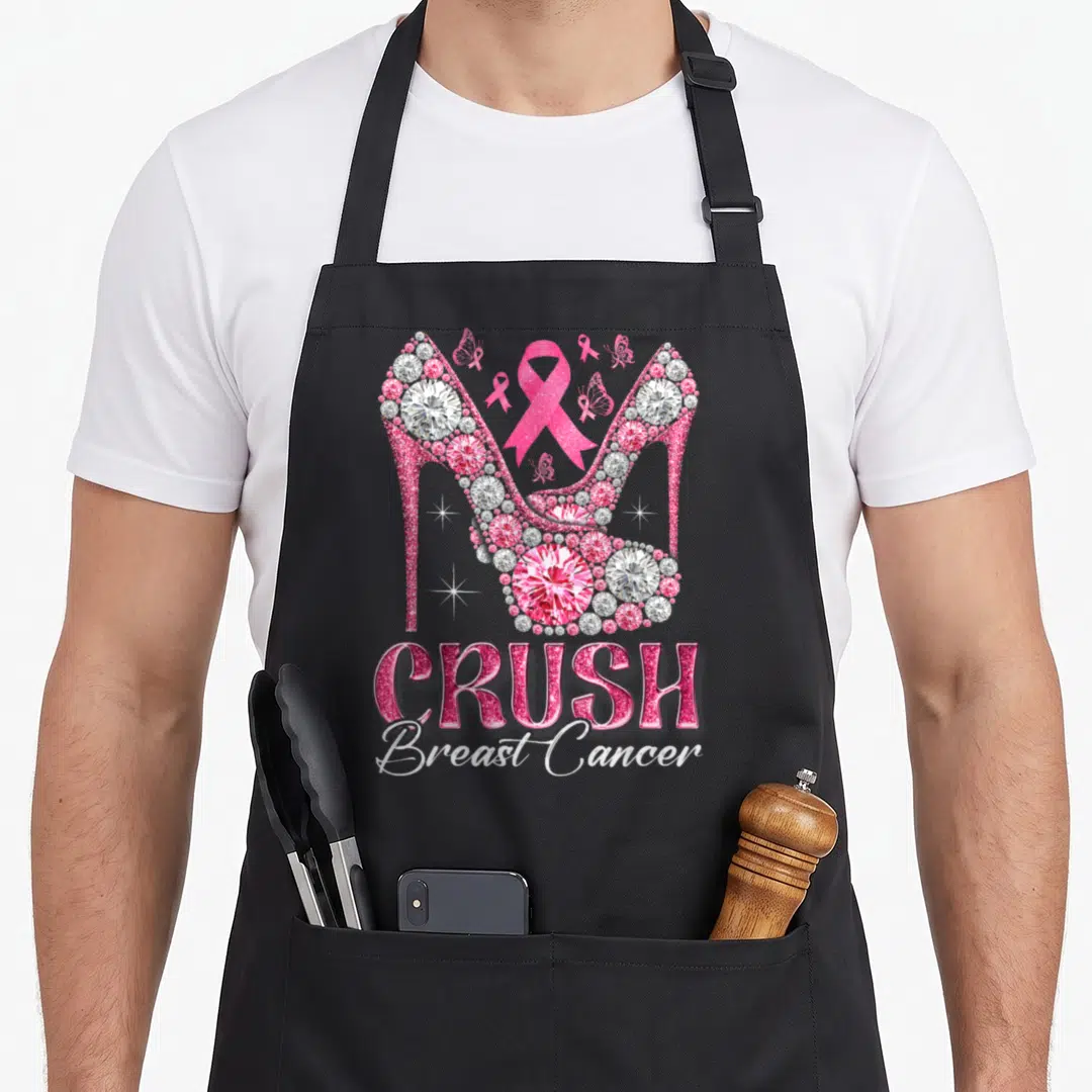 Crush ribbon apron - Two pink diamond high heels with ribbons and CRUSH Breast Cancer text — shown on a black cotton canvas apron against a white background
