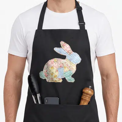 Spring cottage apron - Patchwork rabbit silhouette made of pink floral, blue gingham, and lace fabric pieces — shown on a black cotton canvas apron against a white background
