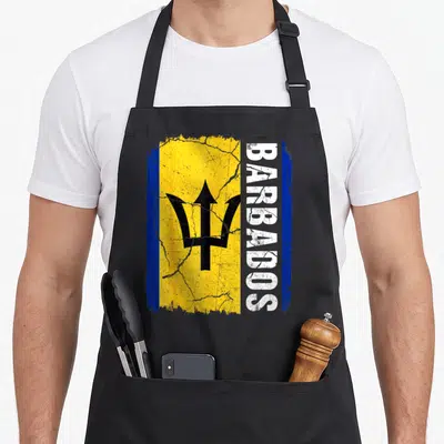 Barbadian flag pride apron - Distressed Barbados flag with vertical white BARBADOS text and black trident on yellow — shown on a black cotton canvas apron against a white background