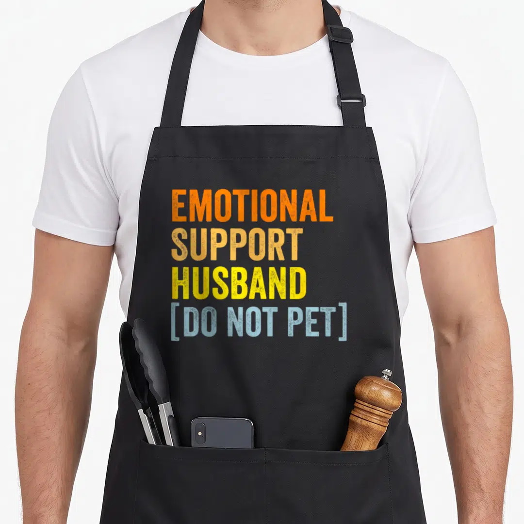 Vintage support husband apron - Stacked orange yellow and blue text reading emotional support husband do not pet — shown on a black cotton canvas apron against a white background