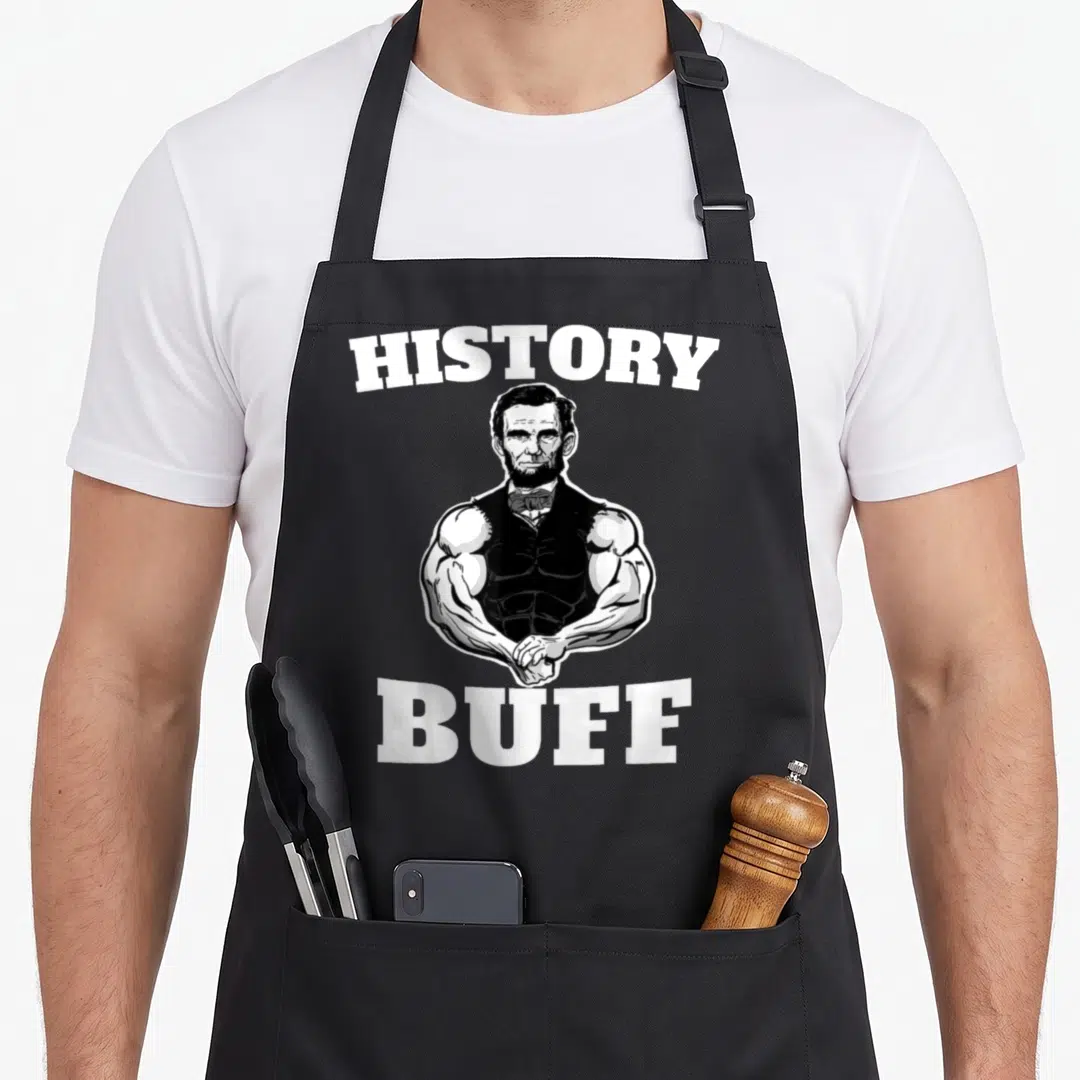 History buff apron - Muscular Abraham Lincoln cartoon between arched HISTORY and straight BUFF text in black and white — shown on a black cotton canvas apron against a white background