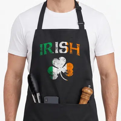 Fade ireland apron - Arched IRISH text in green white orange above a distressed shamrock — shown on a black cotton canvas apron against a white background