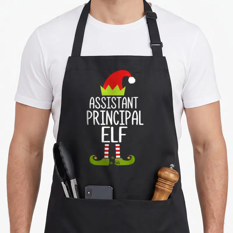 Assistant christmas elf apron - White text body with red hat and green curled shoes between striped legs — shown on a black cotton canvas apron against a white background