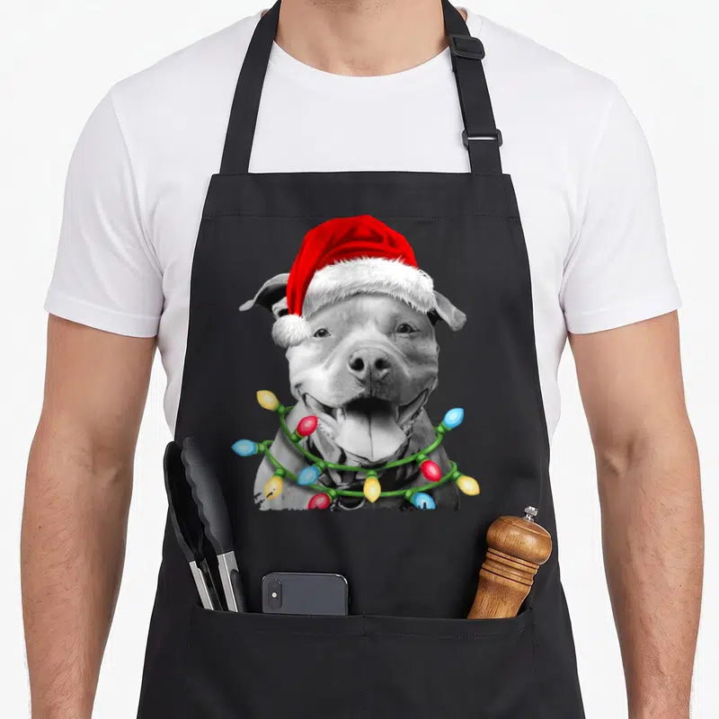 Pit christmas tree apron - Grey dog wearing red santa hat and colorful christmas lights around neck — shown on a black cotton canvas apron against a white background
