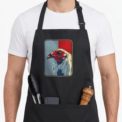 Cockfighting rooster apron - Retro chicken head in rounded frame with split blue and red background and distressed — shown on a black cotton canvas apron against a white background