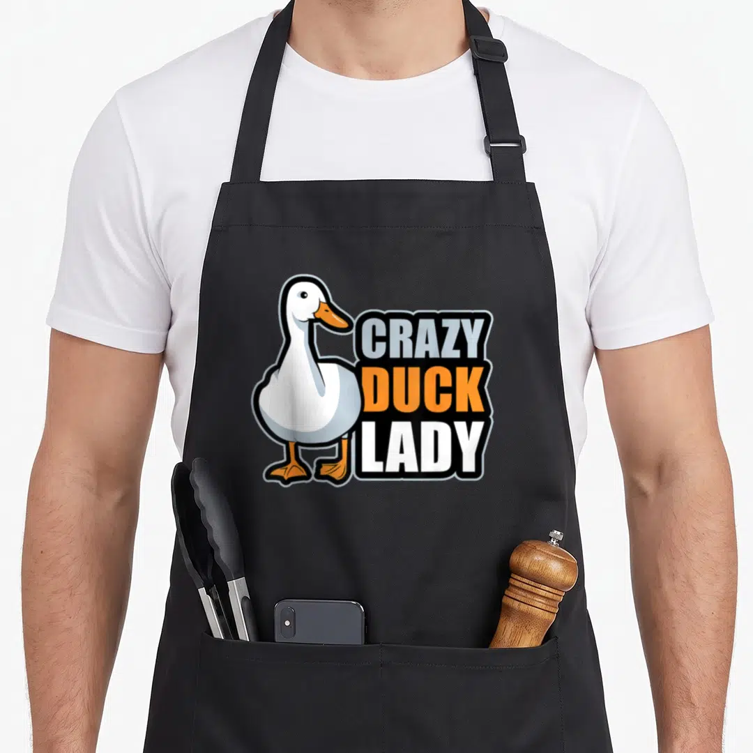 Pekin duck apron - White cartoon duck next to stacked Crazy Duck Lady text in grey and black — shown on a black cotton canvas apron against a white background